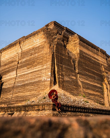 Buddhist monk sitting with red umbrella in front of Mingun Pagoda