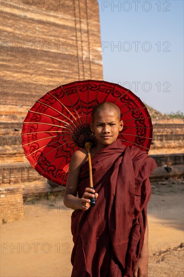 Buddhist monk stands with red umbrella in front of Mingun Pagoda