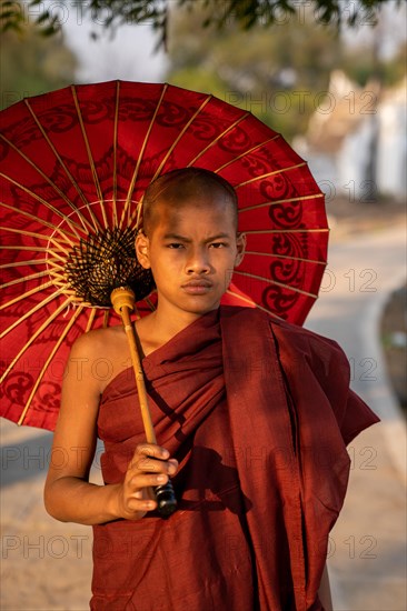 Buddhist monk stands with red umbrella on a path