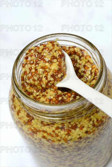 Coarse-grained mustard in glass with spoon