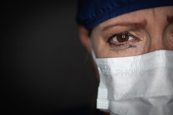 Tearful stressed female doctor or nurse wearing medical face mask on dark background