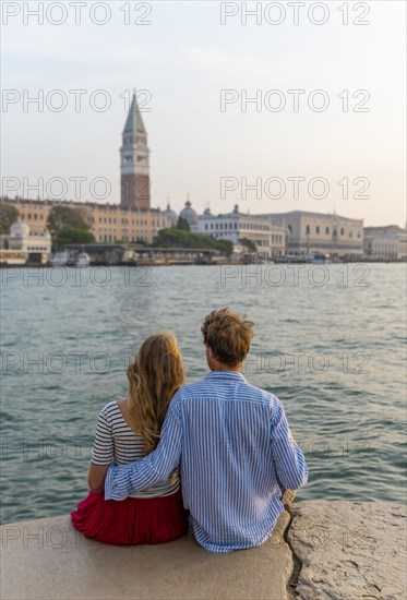 Young couple sitting by the sea enjoying view of St. Mark's Square with Campanile di San Marco