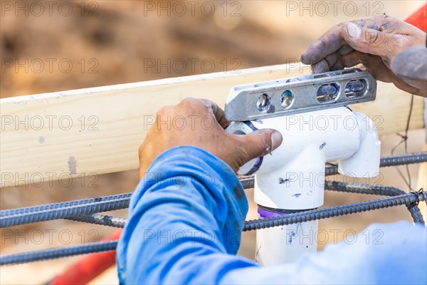 Plumber using level while installing PVC pipe at construction site