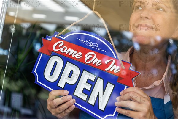 Happy female store owner turning open sign in window