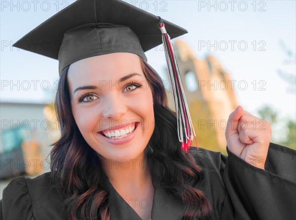 Happy graduating mixed-race woman in black cap and gown celebrating on campus