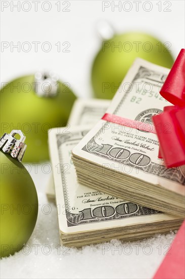 Stack of one hundred dollar bills with red bow near green christmas ornaments on snow flakes