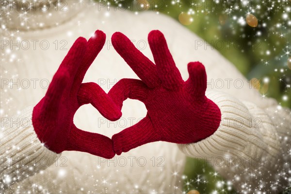 Woman in sweater with seasonal red mittens holding out a heart sign with her hands with snow flakes border