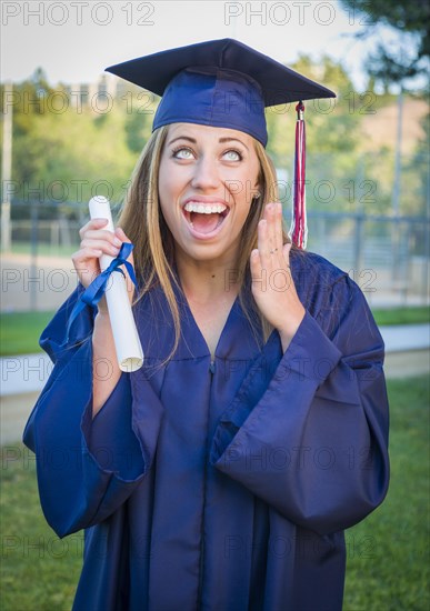 Excited and expressive young woman holding diploma in cap and gown outdoors