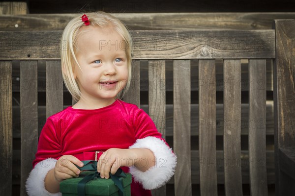 Adorable little girl unwrapping her gift on a bench outside