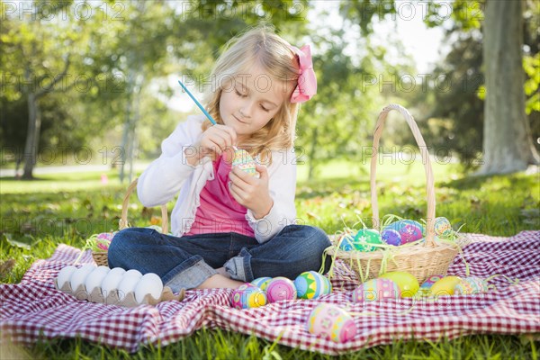 Cute young girl happily coloring her easter eggs with paint brush in the park