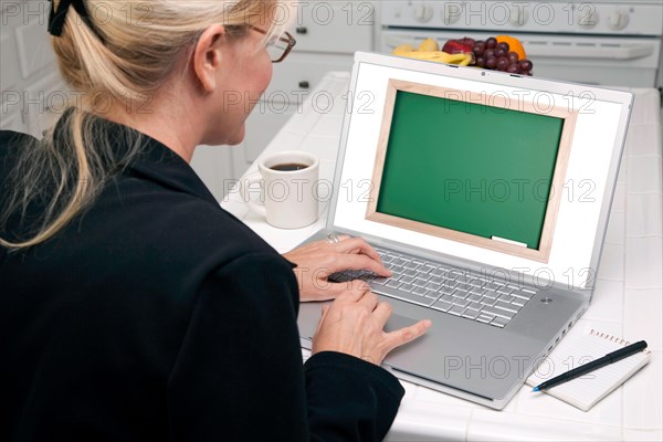 Woman in kitchen using laptop with blank chalkboard ready for you own message. screen can be easily used for your own message or picture. picture on screen is my copyright as well