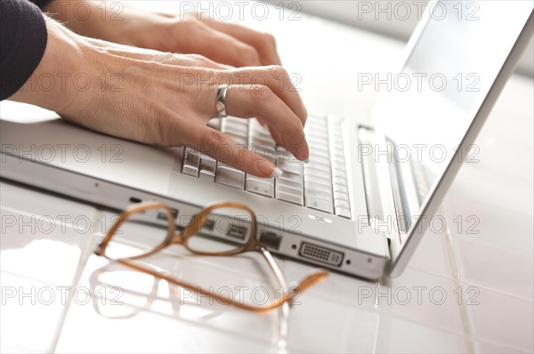 Female hands typing on the keyboard of the laptop with eyeglasses nearby
