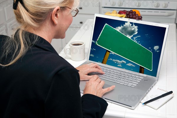 Woman in kitchen using laptop with blank road sign ready for your own message. screen can be easily used for your own message or picture. picture on screen is my copyright as well