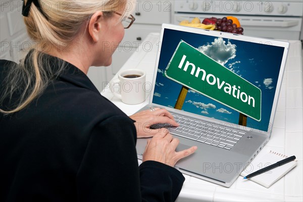 Woman in kitchen using laptop with innovation road sign on screen. screen can be easily used for your own message or picture. picture on screen is my copyright as well