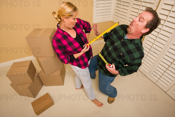 Couple having a fun sword fight with their tape measures surrounded by packed moving boxes