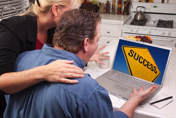 Couple in kitchen using laptop with yellow success road sign on the screen