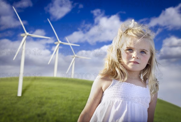 Beautiful young blue eyed girl playing near wind turbines and grass field