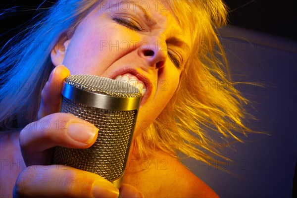 Female vocalist under gelled lighting sings with passion into condenser microphone