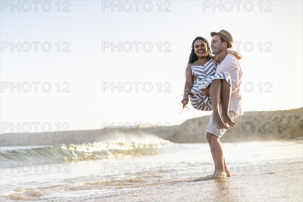 A young man carrying his beloved woman on the beach by sunset in Algarve