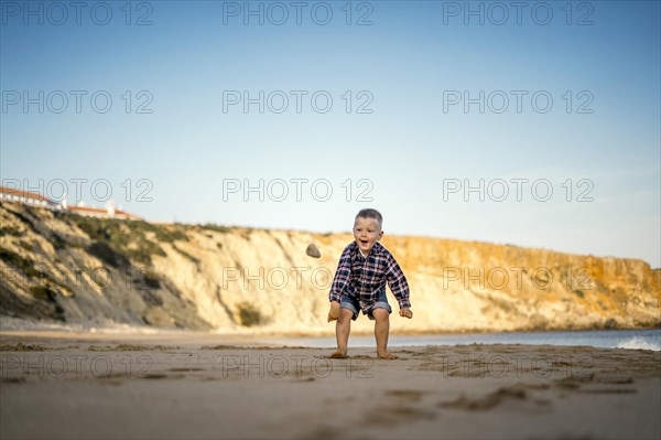 Small boy throwing stones on the beach by the sunset