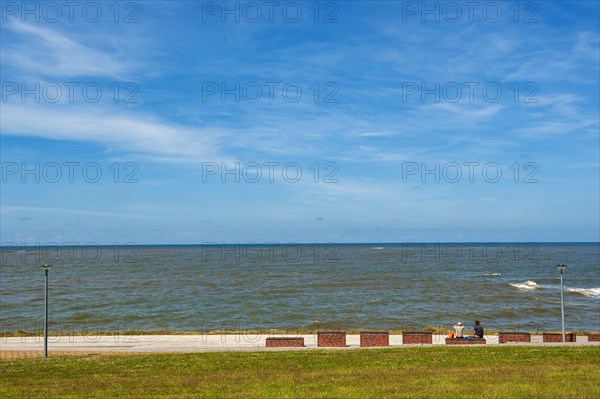 Resting benches with two people at the beach section protected by dikes at the Estdorf of the island Baltrum