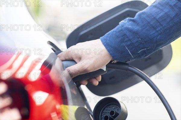 Hand on an electric car charging cable at the car