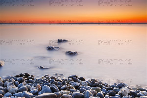 View over Lake Constance at sunrise with stones in the foreground and photographed with slow shutter speed