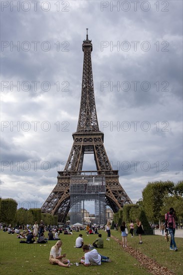 Locals and tourists sitting on a lawn in front of the Eiffel Tower