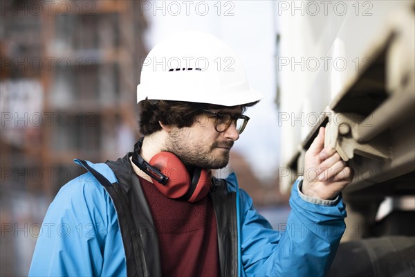 Young engineer wearing a helmet and hearing protection at a work site outside on a construction site