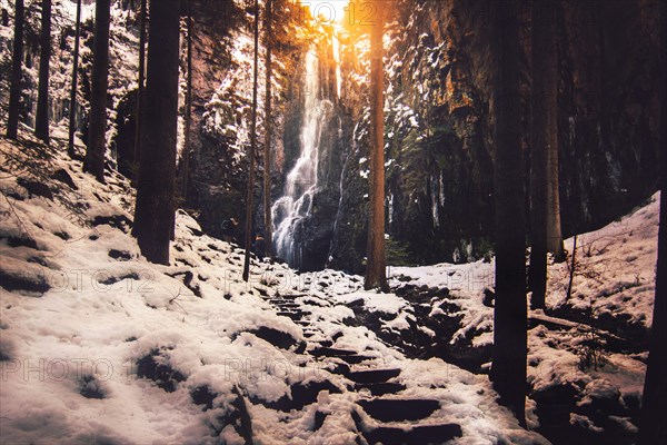 The Burgbach waterfall with snow in winter. Waterfall with stone steps in Schapbach