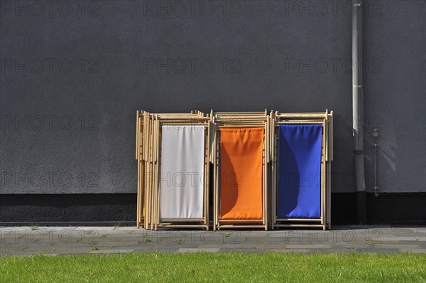 Grey wall with green lawn and coloured deck chairs in park