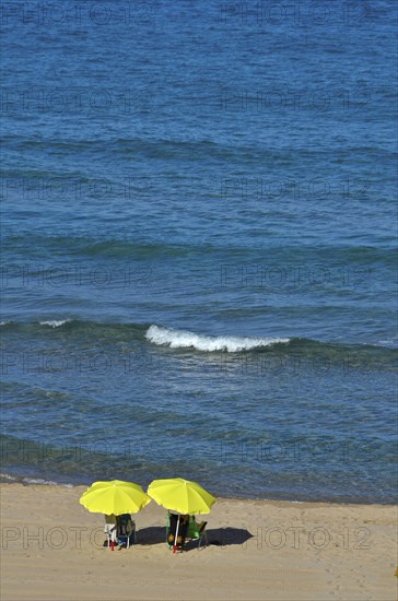 Beachgoers under yellow umbrellas by the sea with wave