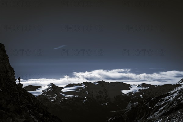 Climber on rocky outcrop with South Tyrolean mountains at blue hour