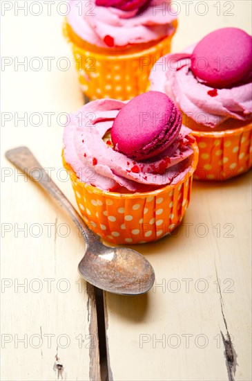 Fresh pink berry cream cupcake with macaroon on top over rustic wood table