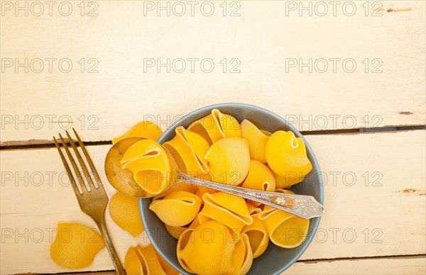 Raw Italian snail lumaconi pasta on a blue bowl over rustic table macro