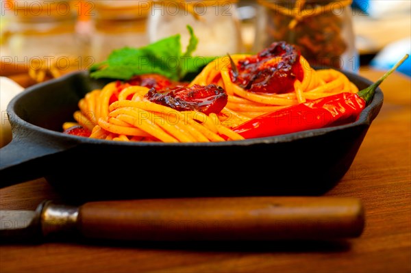 Italian spaghetti pasta and tomato with mint leaves on iron skillet over wood board