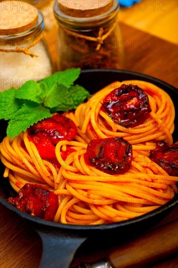 Italian spaghetti pasta and tomato with mint leaves on iron skillet over wood board