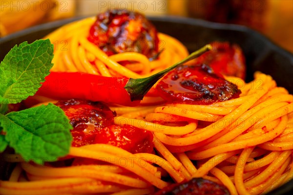 Italian spaghetti pasta and tomato with mint leaves on iron skillet over wood board