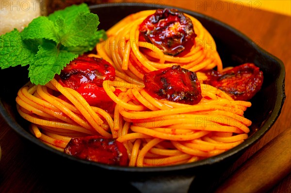 Italian spaghetti pasta and tomato with mint leaves on iron skillet over wood board