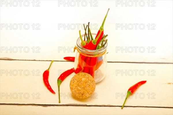 Red chili peppers on a glass jar over white wood rustic table