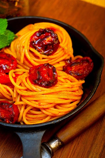 Italian spaghetti pasta and tomato with mint leaves on iron skillet over wood board