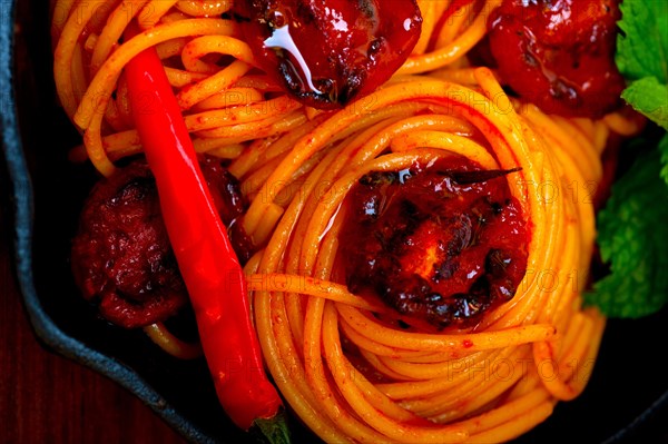 Italian spaghetti pasta and tomato with mint leaves on iron skillet over wood board