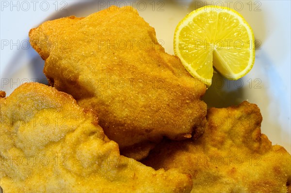 Ready-to-eat Wienerschnitzel with half a lemon on a white plate