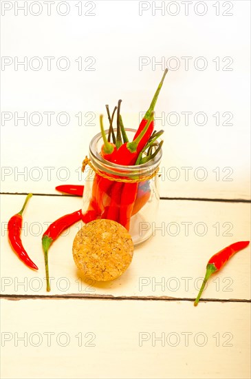 Red chili peppers on a glass jar over white wood rustic table