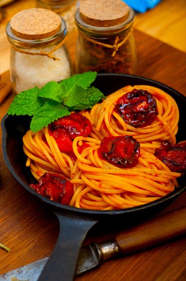 Italian spaghetti pasta and tomato with mint leaves on iron skillet over wood board