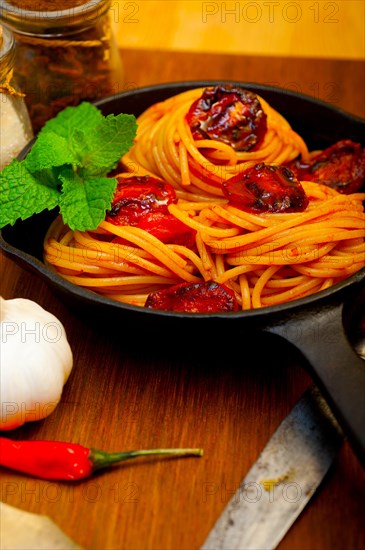 Italian spaghetti pasta and tomato with mint leaves on iron skillet over wood board