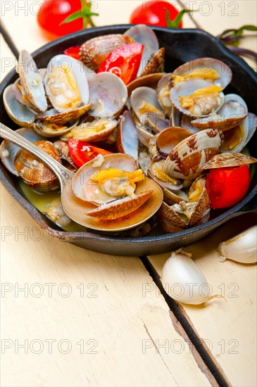 Fresh clams stewed on an iron skillet over wite rustic wood table