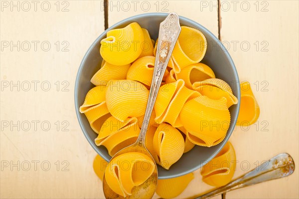 Raw Italian snail lumaconi pasta on a blue bowl over rustic table macro