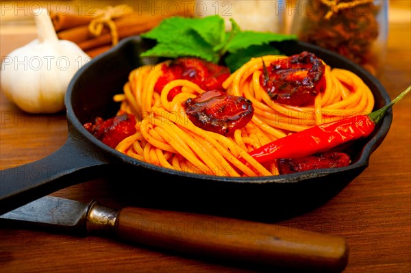 Italian spaghetti pasta and tomato with mint leaves on iron skillet over wood board