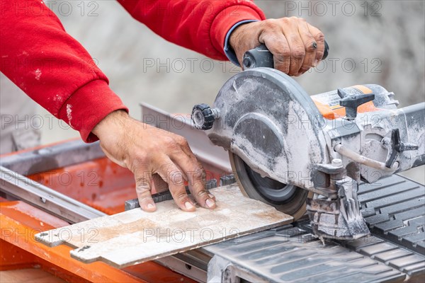 Worker using wet tile saw to cut wall tile at construction site